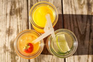 Enjoy top-down view of citrus and strawberry drinks with ice in jars on wooden table.