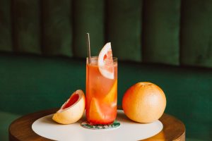 Glass of grapefruit cocktail with fresh slices on table, ideal for refreshing summer drinks.